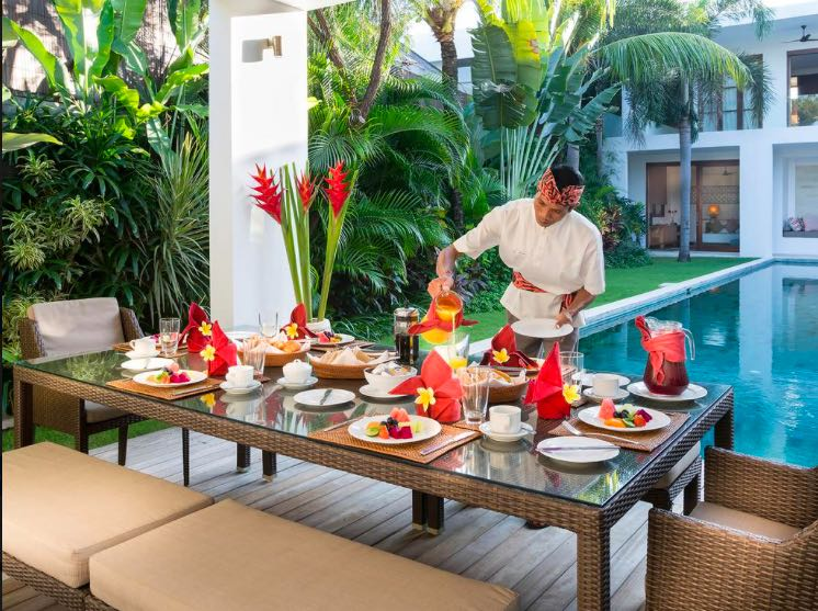 Chef setting breakfast beside a villa pool
